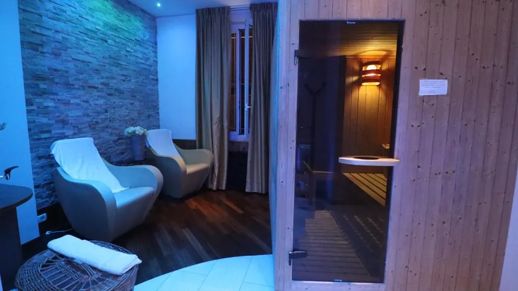 Zona relax della spa con poltrone, parete in pietra, illuminazione blu e ingresso alla sauna in legno