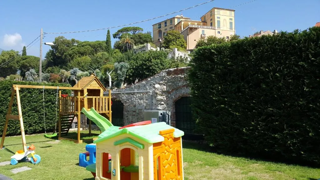 Giardino con area giochi per bambini, scivolo e casetta, antiche mura sullo sfondo