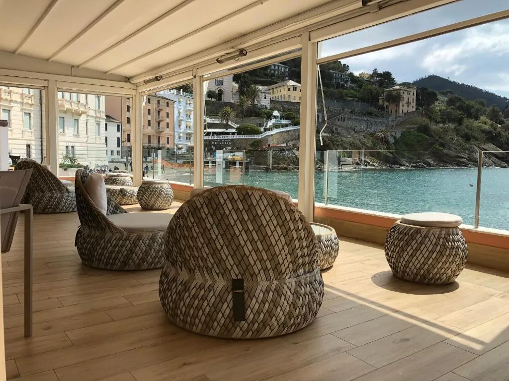 Lounge con poltrone in rattan e vetrate panoramiche affacciate sulla baia e sulla collina