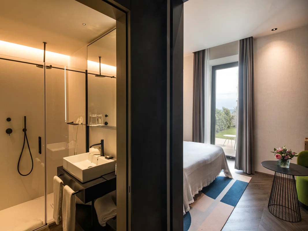 Camera con bagno open space dotato di doccia in vetro, lavabo e accesso al terrazzo con vista