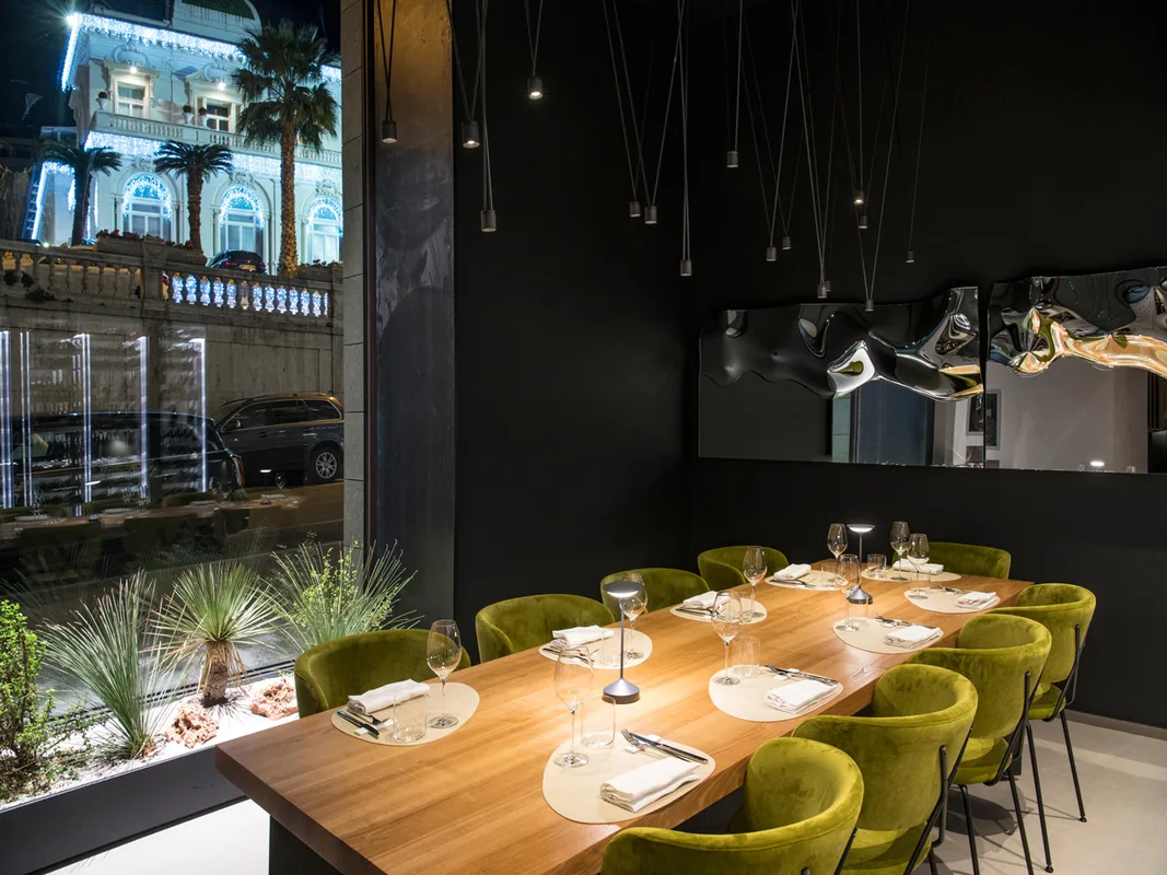 Sala ristorante elegante con tavolo in legno, sedie verdi in velluto e vista sulla città illuminata