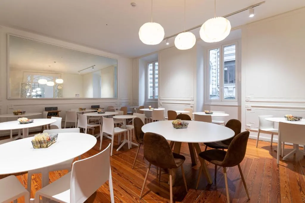 Sala colazione luminosa con tavoli rotondi bianchi, sedie, grande specchio e lampade a sospensione