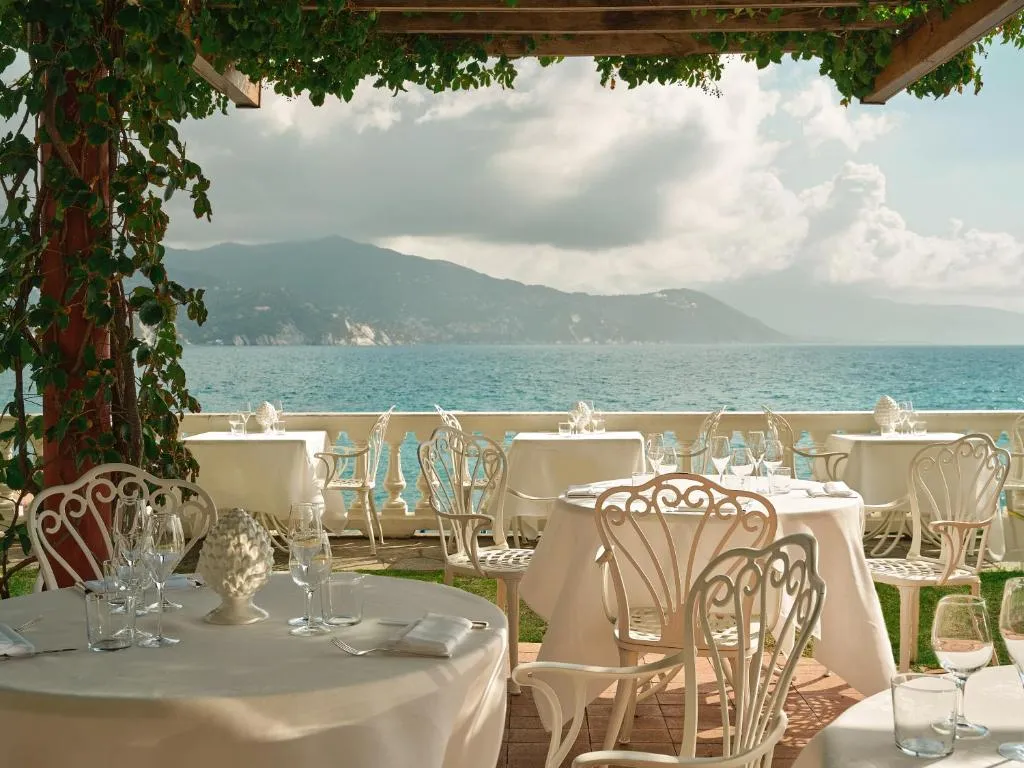 Terrazza ristorante con tavoli apparecchiati, sedie bianche in ferro battuto e vista panoramica sul mare e le montagne
