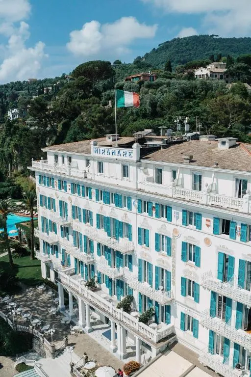 Facciata dell'hotel Miramare con bandiera italiana, persiane azzurre e architettura storica circondata dal verde