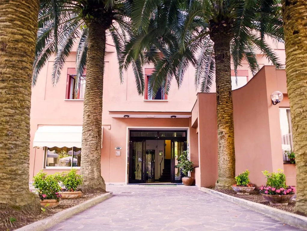 Ingresso dell'hotel con viale fiancheggiato da alte palme e facciata rosa