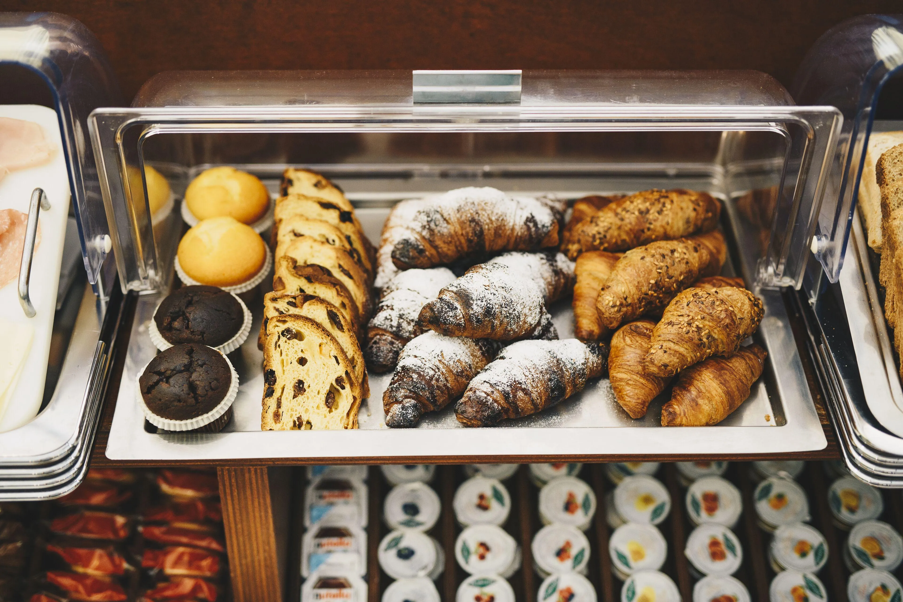 Vassoio del buffet con cornetti, muffin al cioccolato, plumcake e vaschette di confettura