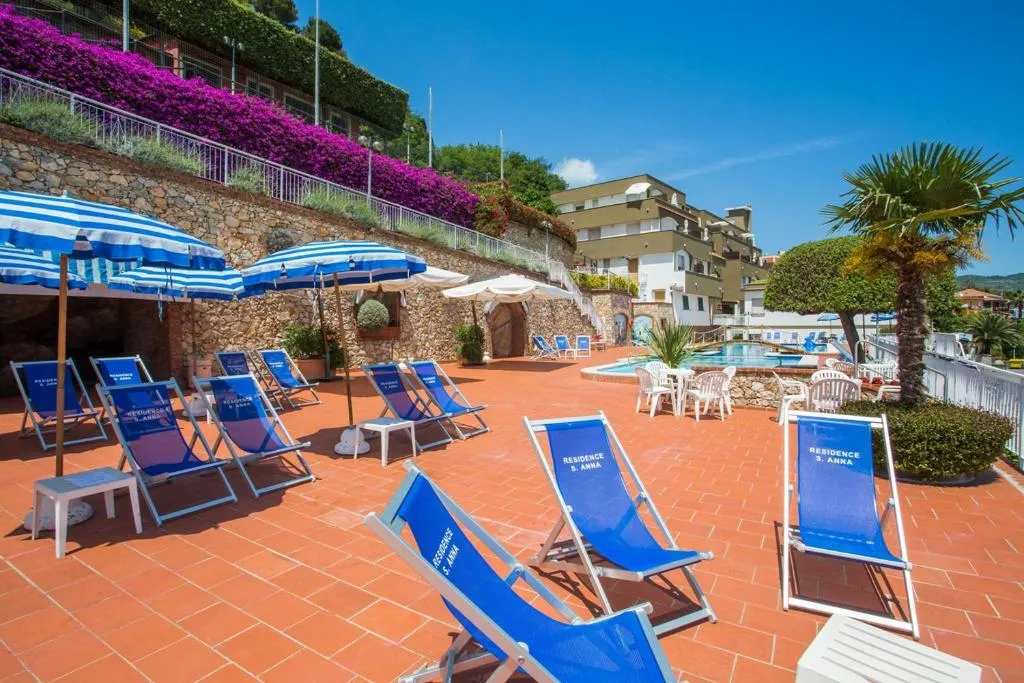 Terrazza solarium con lettini e ombrelloni blu, tavoli, piscina, palme e bouganville fiorite