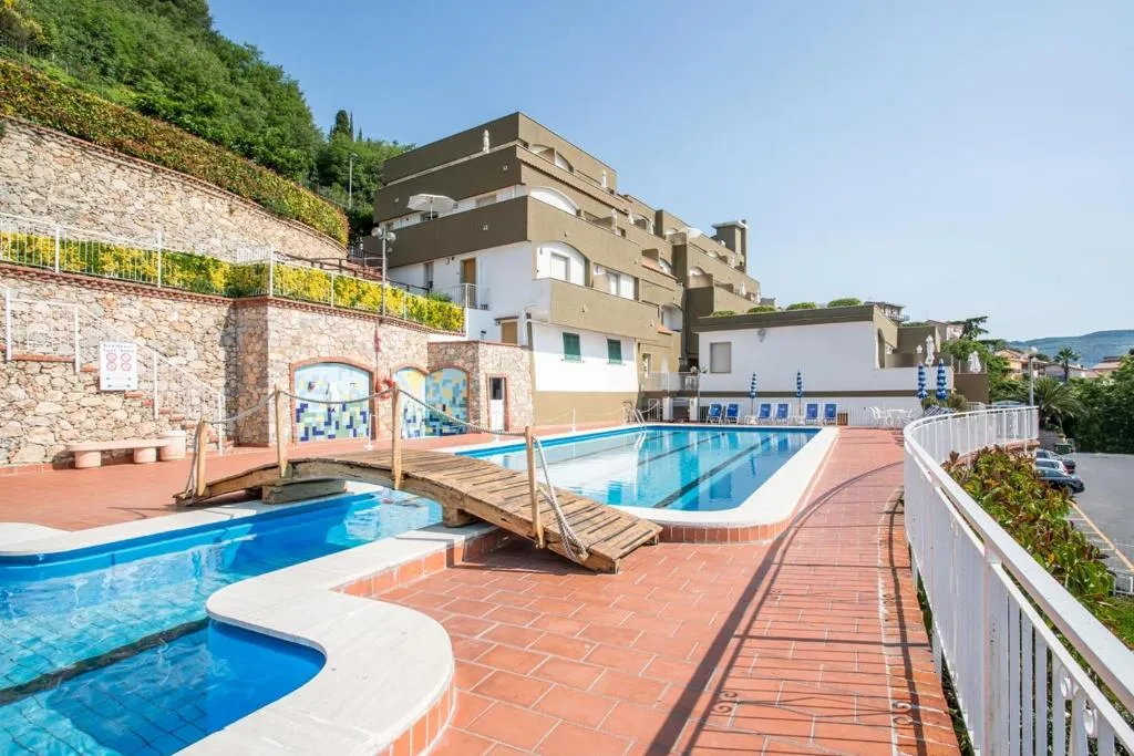 Complesso residenziale con piscine collegate da ponticello in legno, terrazza in cotto e muri in pietra