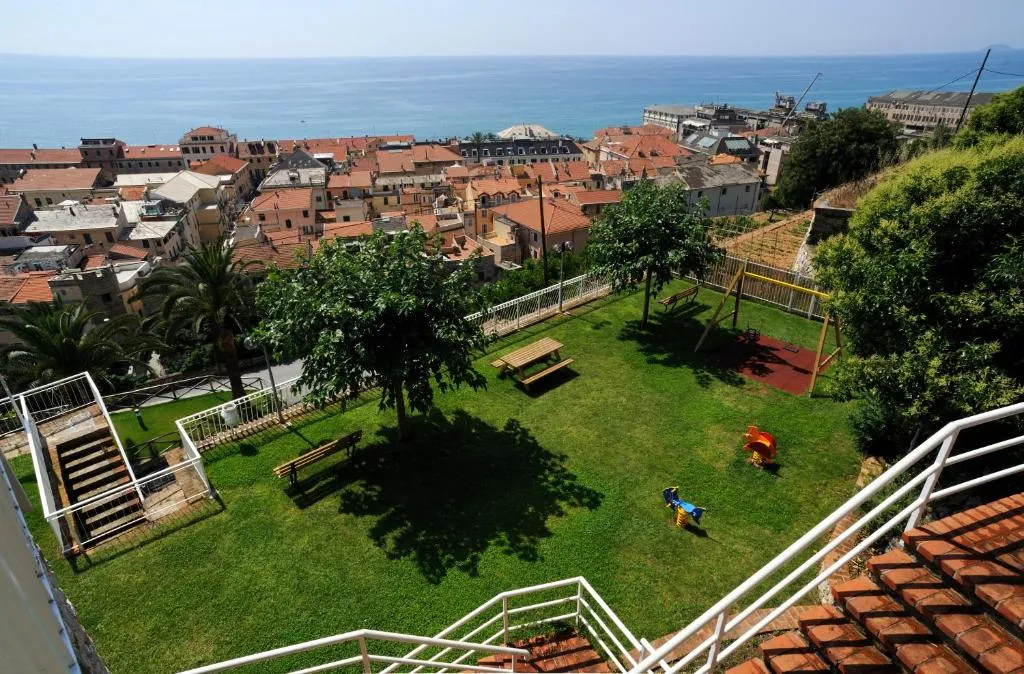 Vista panoramica dall'alto sul paese, sui tetti rossi, sul mare e su giardino con parco giochi e palme