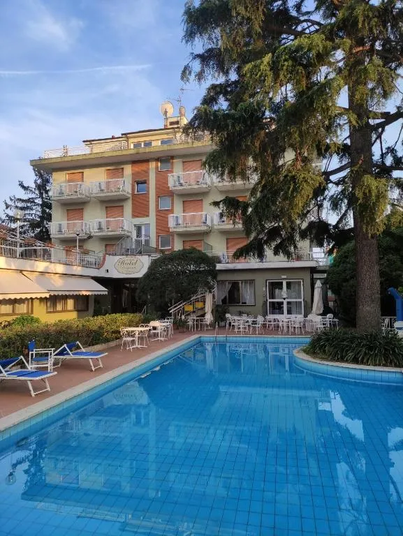 Esterno dell'hotel con piscina, lettini, tavolini e pino in primo piano