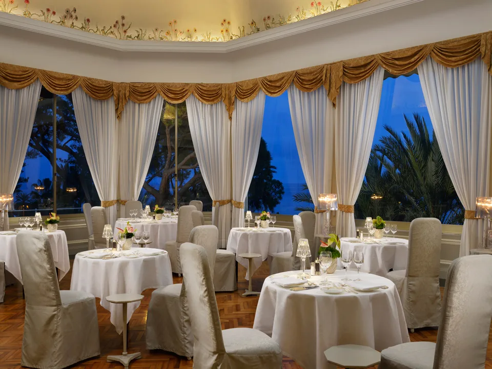 Sala ristorante elegante con tavoli rotondi bianchi, tende dorate e vista serale sul giardino