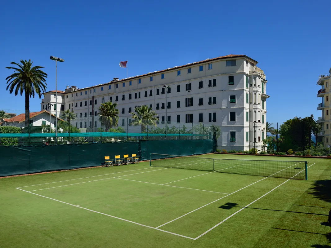 Campo da tennis in erba sintetica con la facciata dell'hotel sullo sfondo