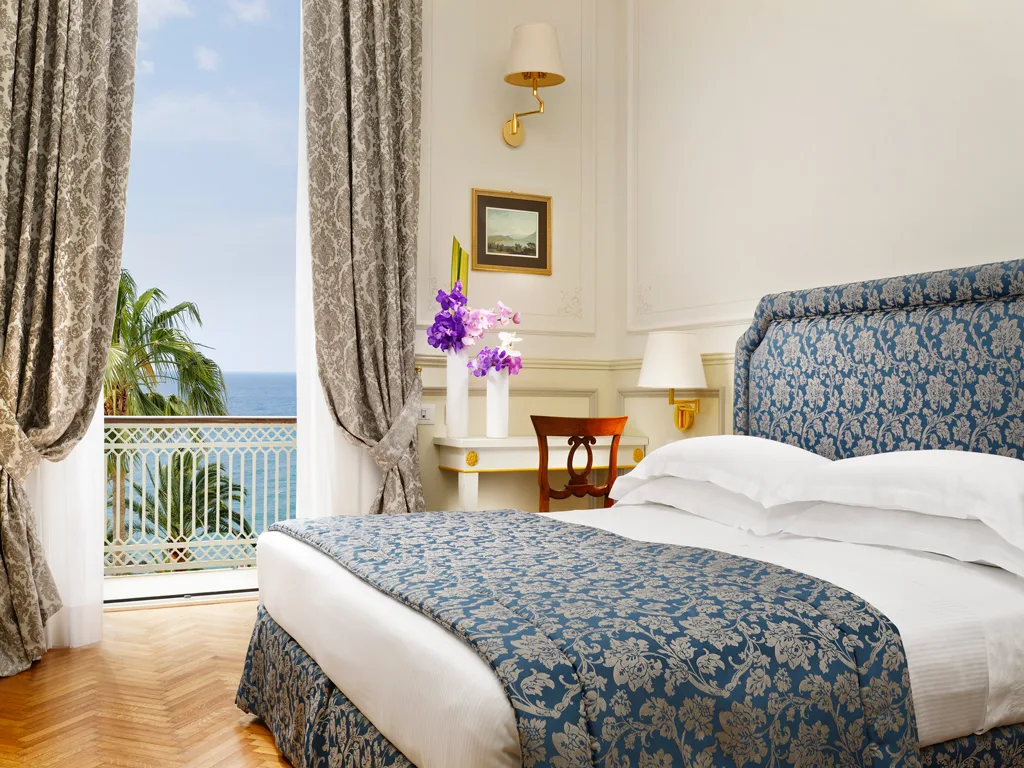 Camera elegante con testiera blu damascata, balcone e vista sul mare