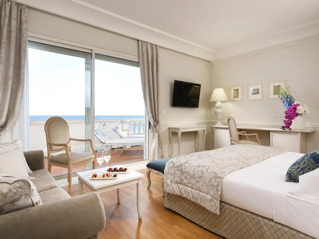 Camera elegante con divano, scrivania e ampia vetrata con accesso alla terrazza vista mare