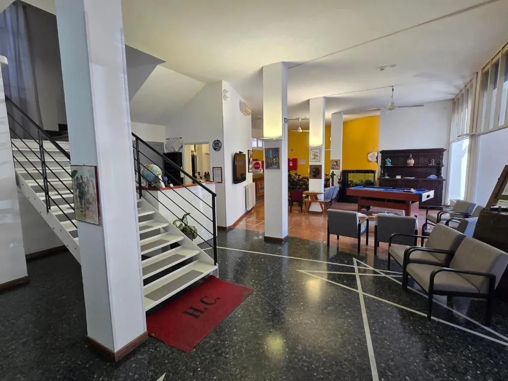Hall con scala bianca, zona salotto con poltrone e tavolo da biliardo