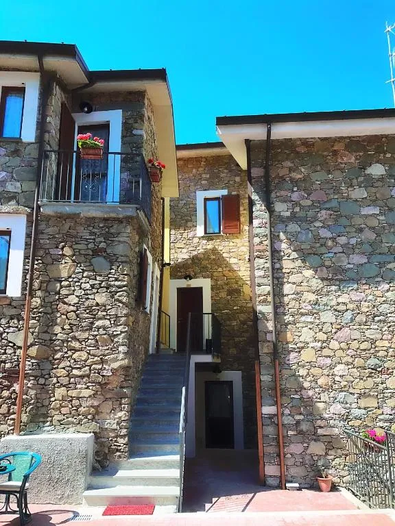 Scalinata esterna in pietra tra edifici con balconi fioriti e cielo azzurro