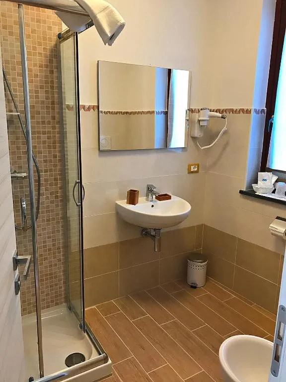 Bagno con doccia in vetro, lavabo sospeso, specchio e pavimento effetto legno