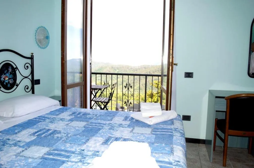 Camera con letto matrimoniale, scrivania e balcone aperto con vista panoramica sulle colline