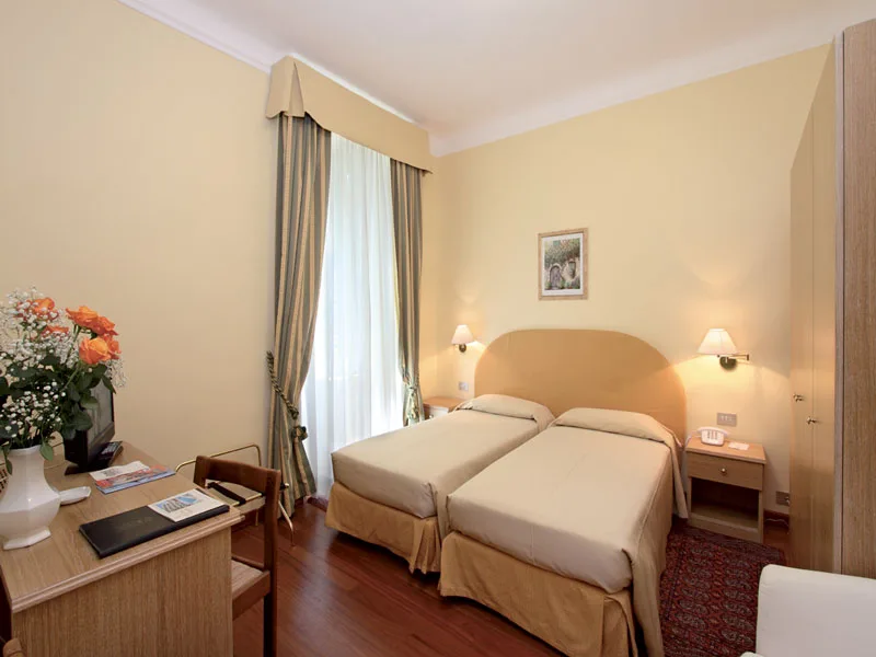 Camera con due letti singoli, scrivania e finestra con tende a righe
