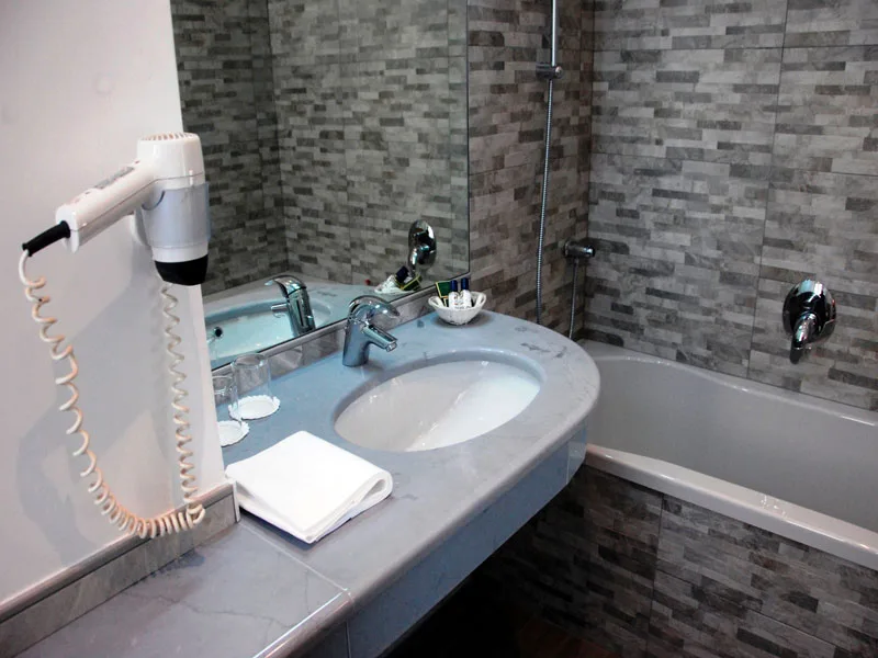 Bagno con lavabo in marmo, specchio, asciugacapelli e vasca con rivestimento a mosaico