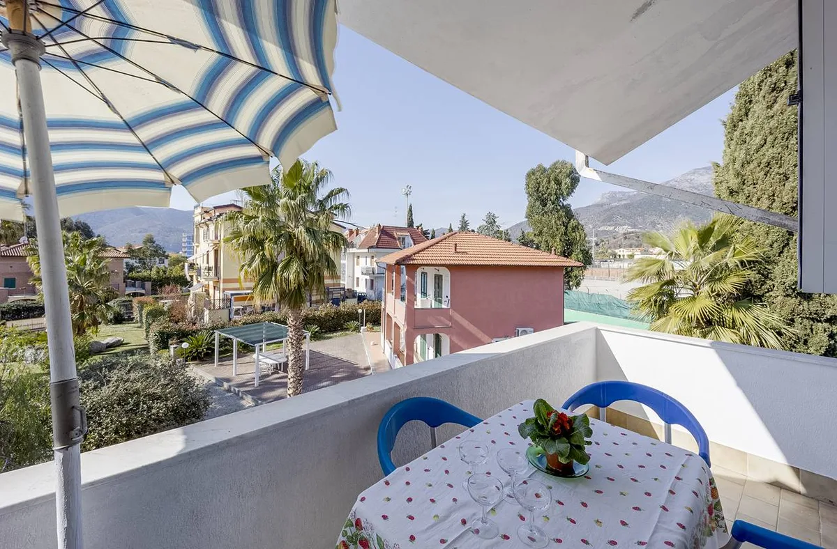 Balcone con tavolo apparecchiato, ombrellone e vista su giardino e colline