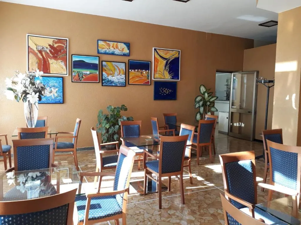 Sala colazione con tavoli in vetro, sedie blu e quadri colorati alle pareti