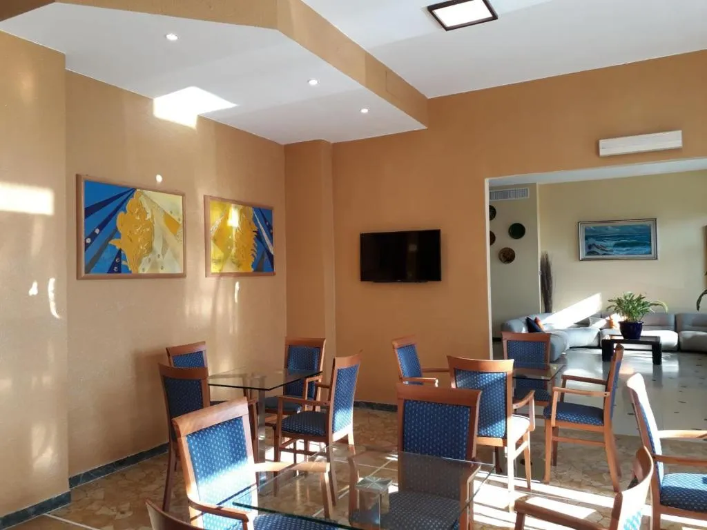 Sala soggiorno con tavoli in vetro, sedie blu, TV e quadri colorati alle pareti