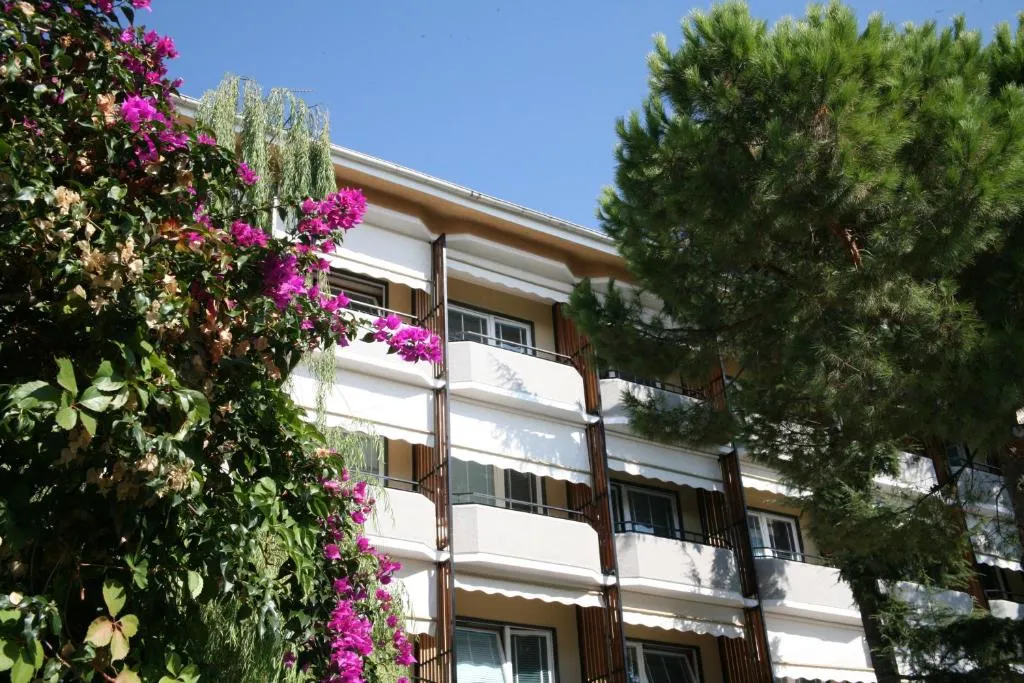 Esterno dell'hotel con balconi, alberi e bougainvillea fiorita