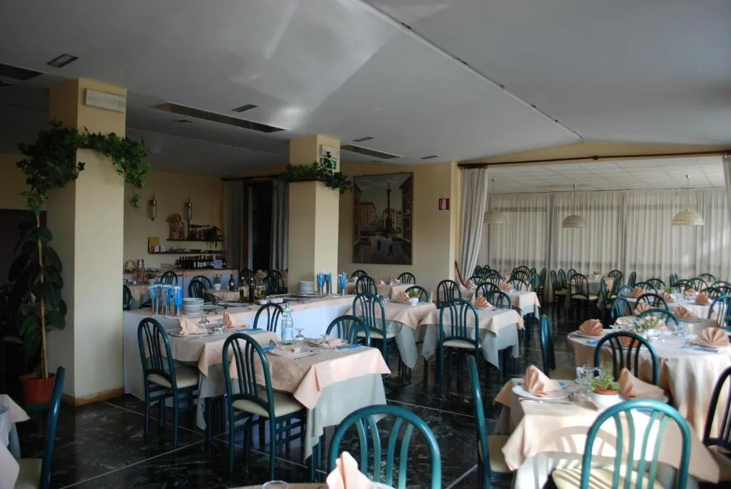 Sala ristorante con tavoli apparecchiati, sedie verdi e pavimento scuro