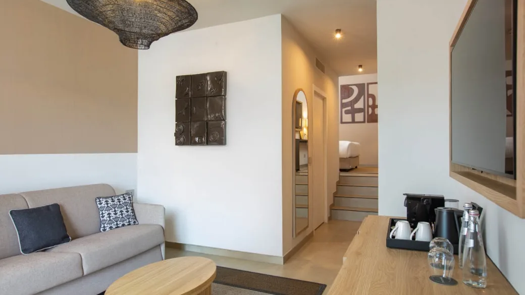 Interno di suite con zona soggiorno, divano e camera da letto rialzata con gradini