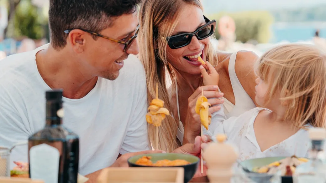 Famiglia sorridente che pranza all'aperto gustando piatti tipici