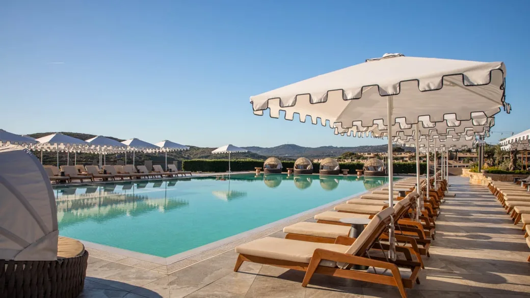 Piscina con lettini e ombrelloni bianchi affacciata sulle colline della Sardegna