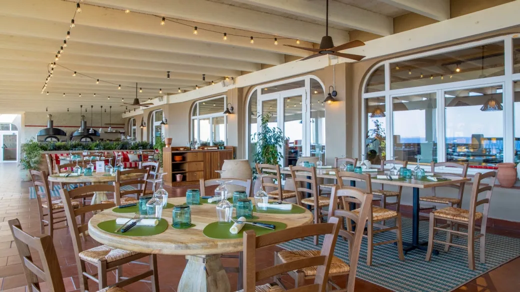 Ristorante con forno a legna, tavoli rotondi in legno e ampie vetrate