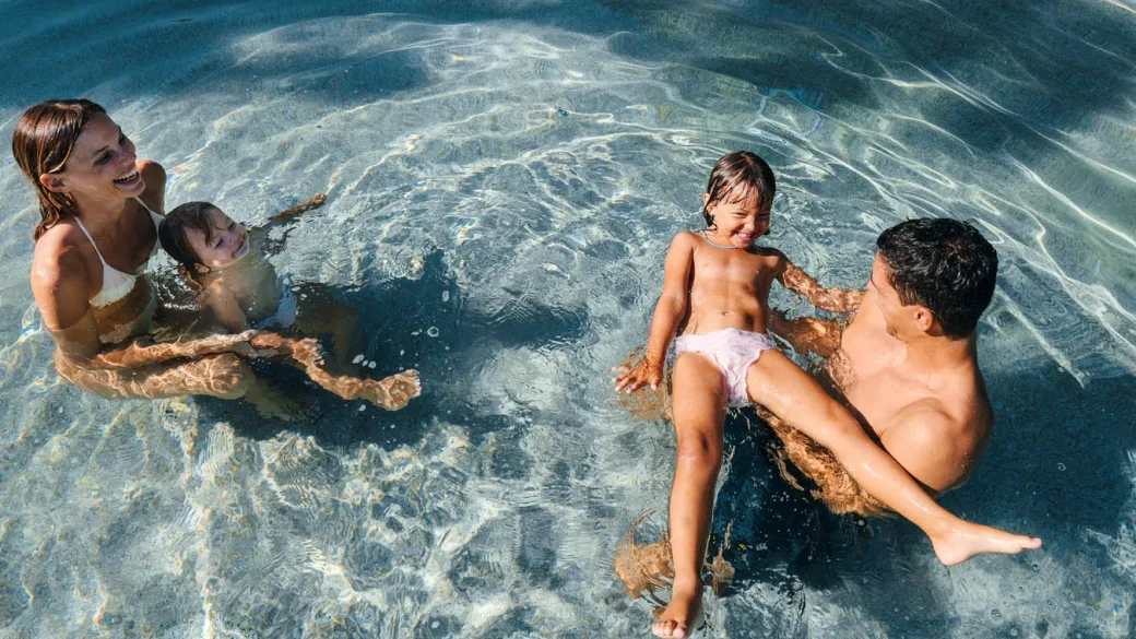 Famiglia che gioca felice nell'acqua cristallina della piscina