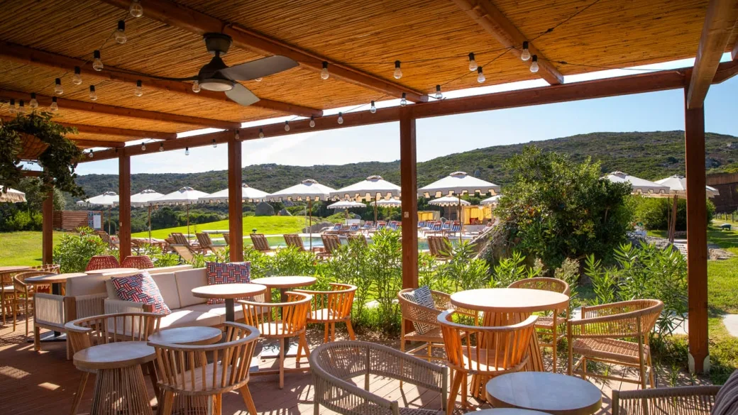 Area lounge sotto pergolato in legno con poltrone in rattan e vista sulla piscina