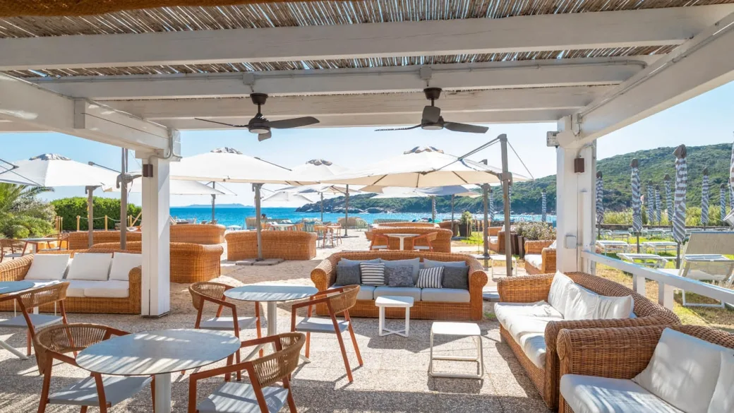 Bar sulla spiaggia con divani in rattan, ombrelloni bianchi e vista mare