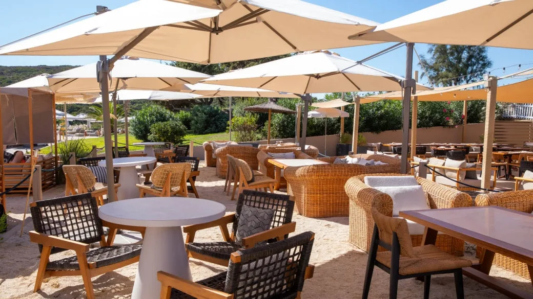 Lounge esterno con poltrone in rattan e ombrelloni sulla sabbia