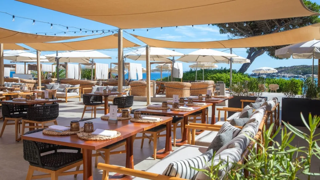 Ristorante all'aperto con tende, tavoli e divani affacciato sul mare