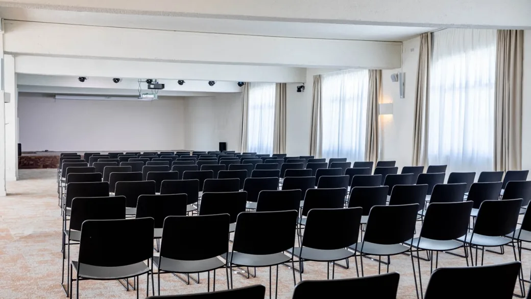 Sala conferenze con file di sedie nere e ampie finestre con tende