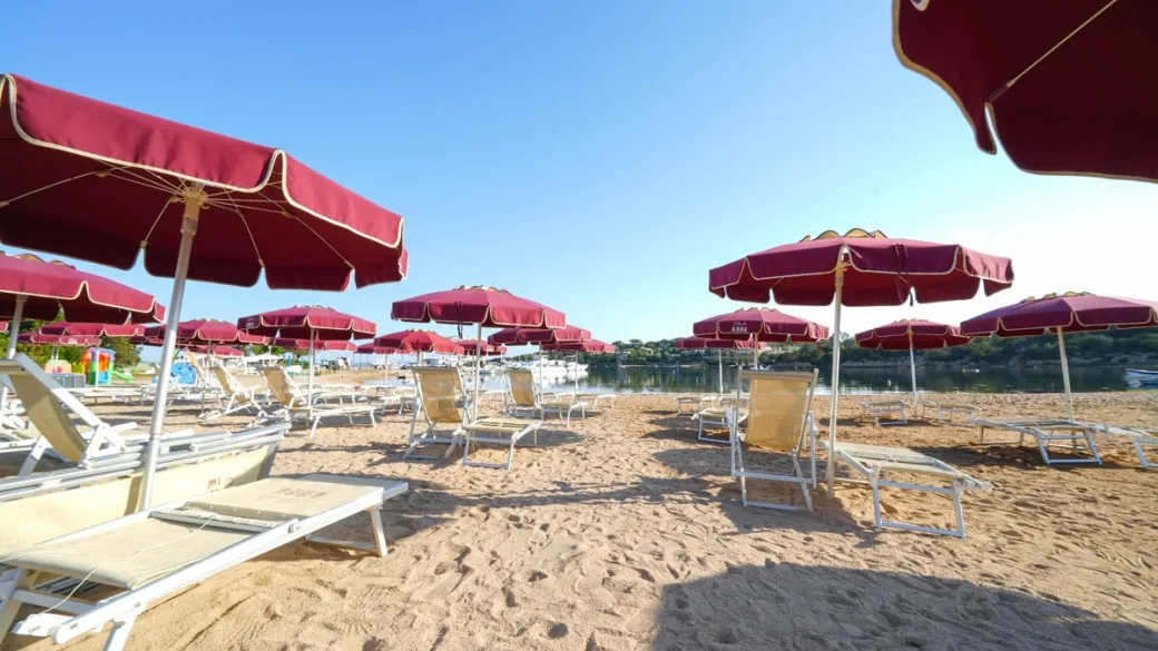 Spiaggia attrezzata con ombrelloni rossi e lettini vista mare