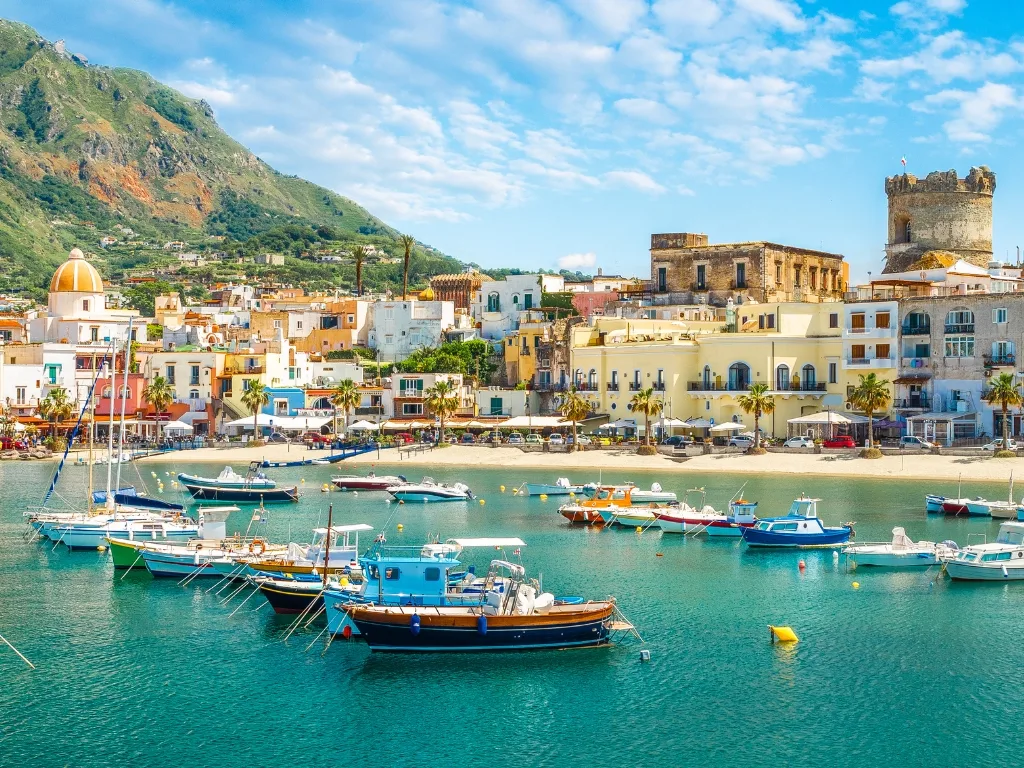 Porticciolo di Ischia con barche colorate, edifici storici e montagne sullo sfondo