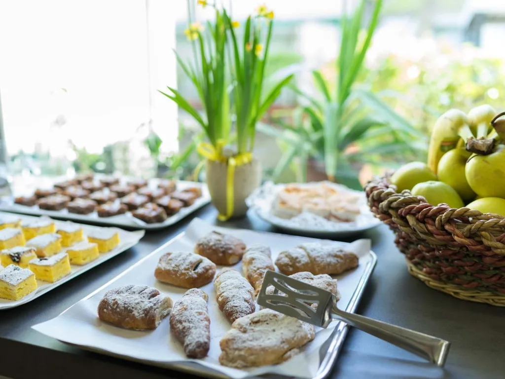 Buffet con dolci, paste e cesto di frutta fresca vicino alla finestra
