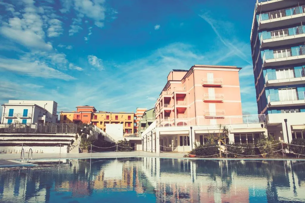 Esterno della struttura con edifici colorati e piscina riflettente sotto cielo azzurro