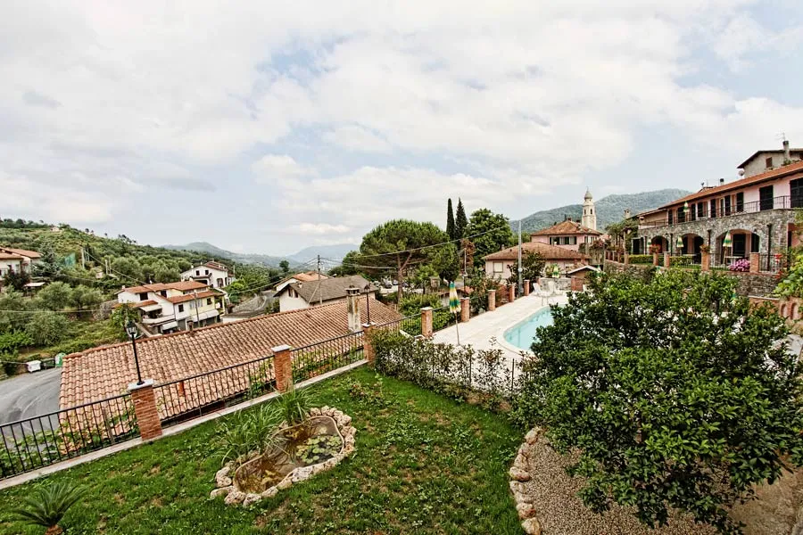 Vista panoramica sul borgo collinare con giardino, piscina e montagne sullo sfondo