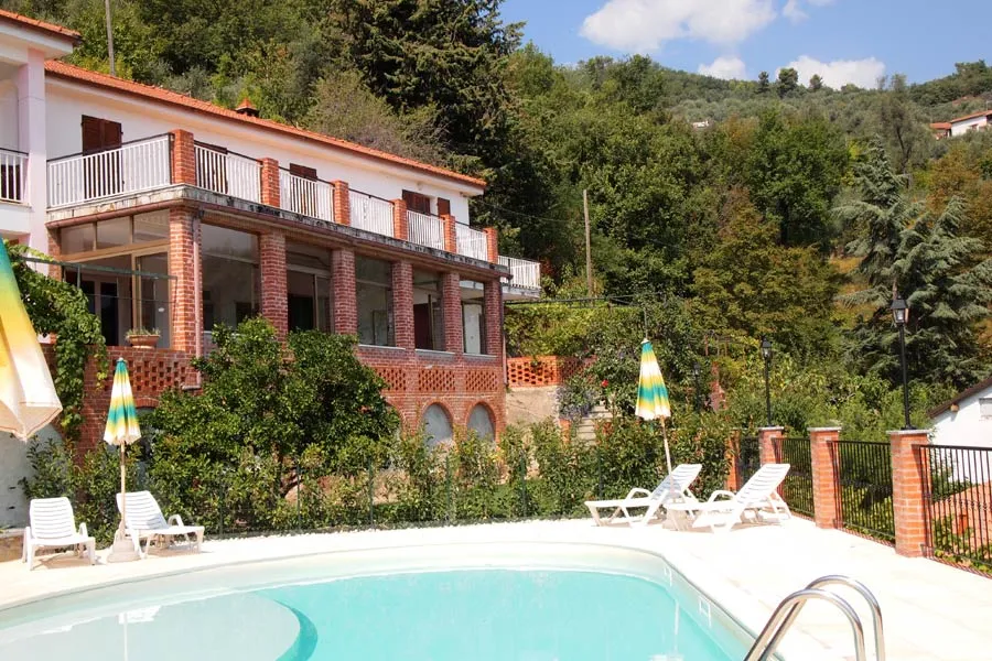 Piscina esterna con lettini e ombrelloni accanto a una villa immersa nel verde collinare