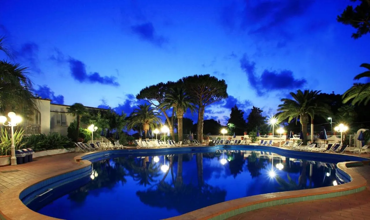 Piscina esterna al crepuscolo con palme illuminate e cielo blu intenso