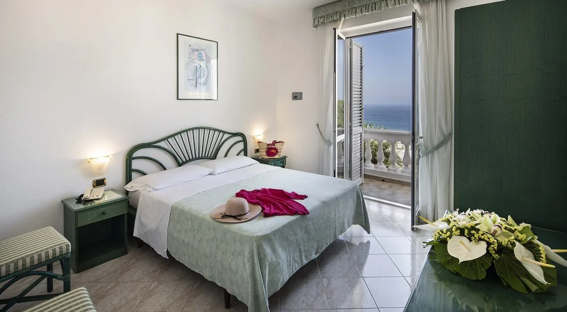 Camera matrimoniale con vista mare dal balcone e arredi verdi in vimini